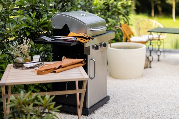 Ein Gasgrill aus Edelstahl steht mit Zubehör in einem Garten.